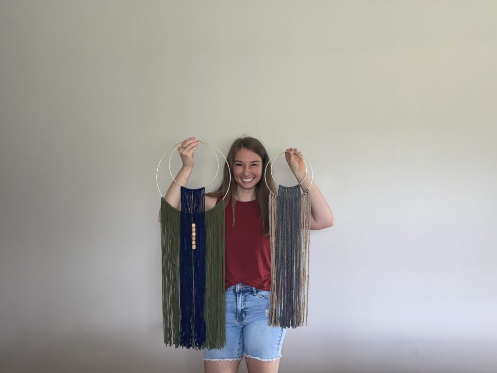 a woman holding two macrame wall hangings homemade
