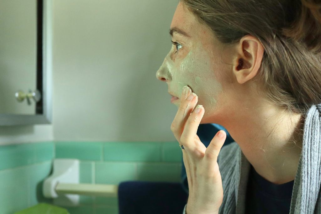 a woman applying a bentonite clay mask to her face with her finger